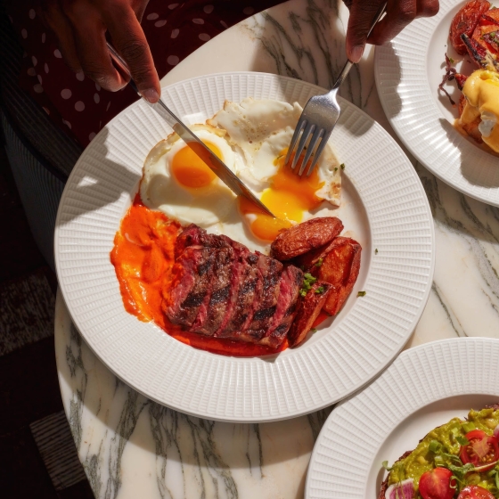 A woman breaks into a runny yolk on a plate of breakfast