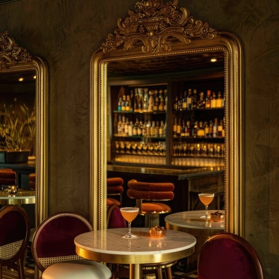 A small table with elegant chairs at Darling. A cocktail is placed on the table and a view of the bar is seen through a mirror behind the setting.