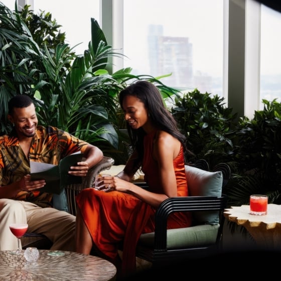 A couple drinks cocktails while perusing a restaurant menu.