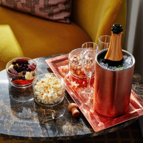 A bottle of chilled champagne, popcorn, nuts and dried fruit on a display tray.