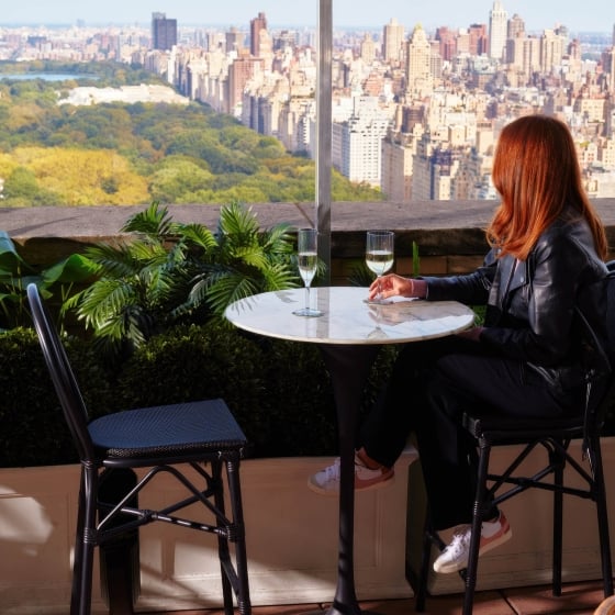 A woman drinks a glass of wine while looking at the view over Central Park.