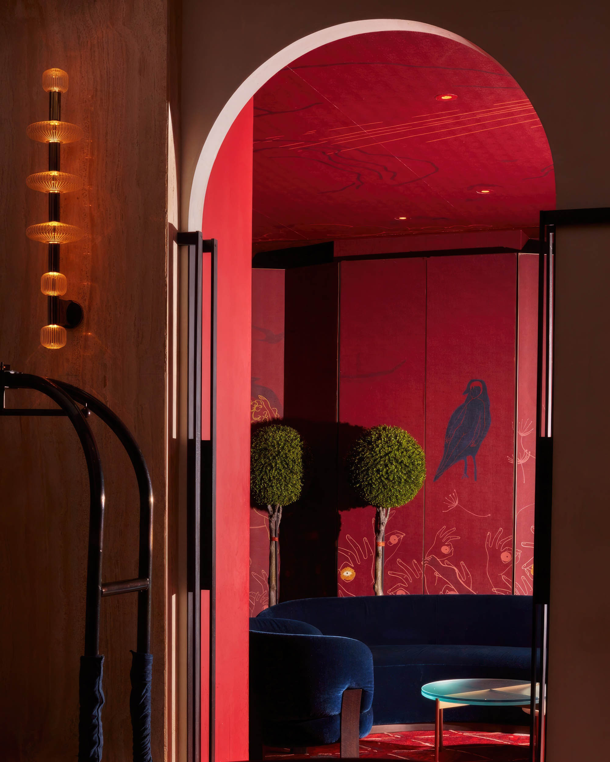 A lounge area with red walls and ceiling and blue velvet couch.