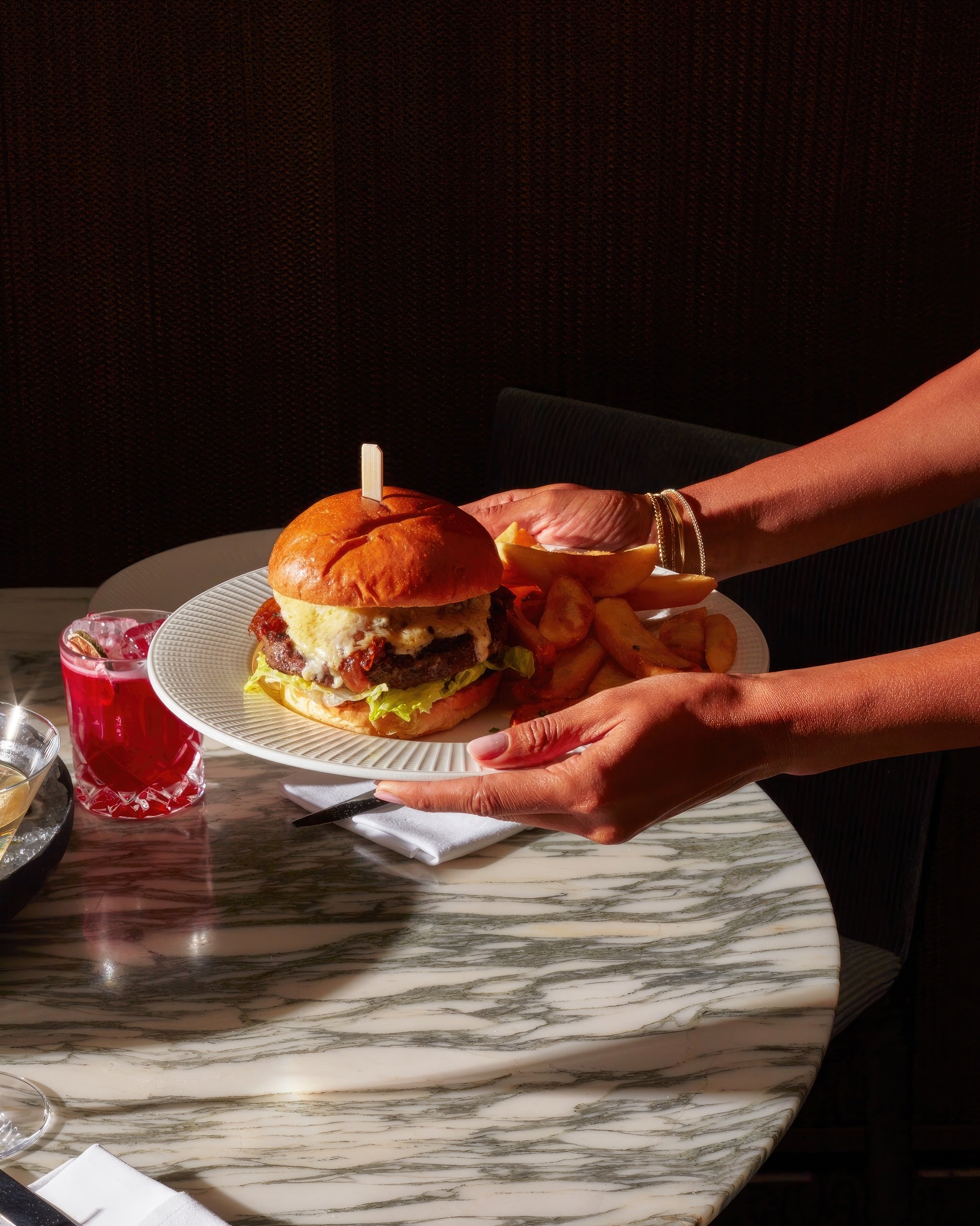 A woman holds a plate with a cheese burger.