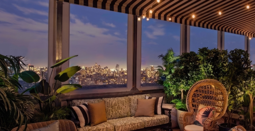 A cozy lounge area with warm lighting at dusk, New York City skyline in the background.