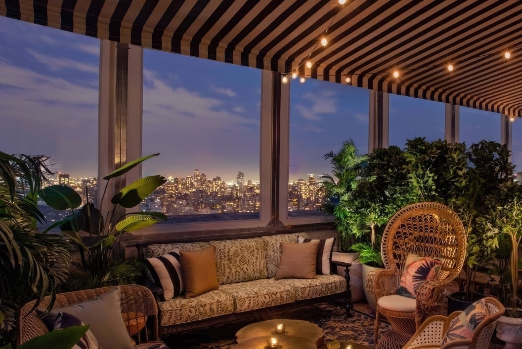 A cozy lounge area with warm lighting at dusk, New York City skyline in the background.