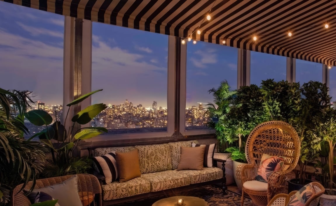 A cozy lounge area with warm lighting at dusk, New York City skyline in the background.