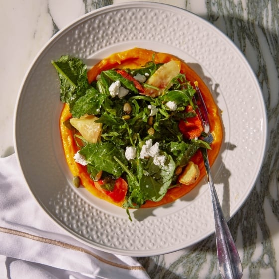 A plate of leafy greens on an orange pureed base.