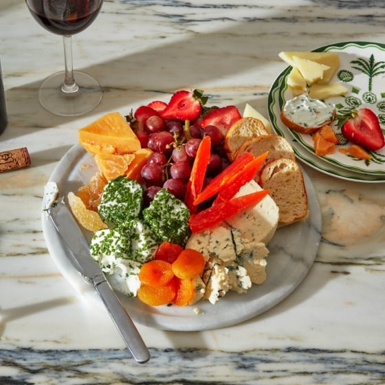 A plate of cheeses, mixed fresh and dried fruit, with a glass of red wine.