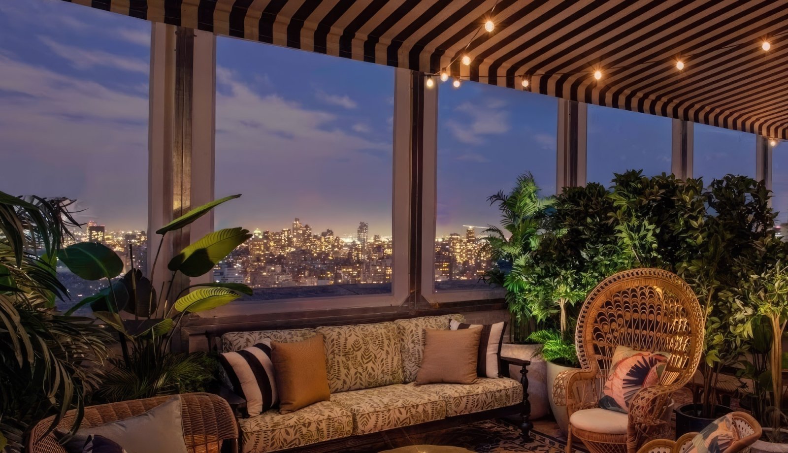 A cozy lounge area with warm lighting at dusk, New York City skyline in the background.