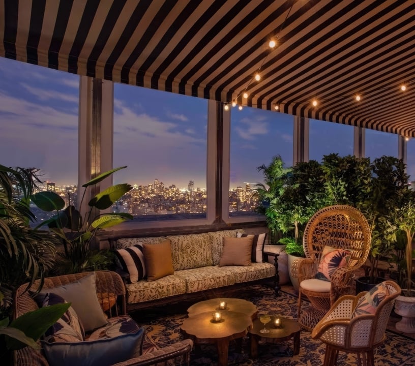 A cozy lounge area with warm lighting at dusk, New York City skyline in the background.