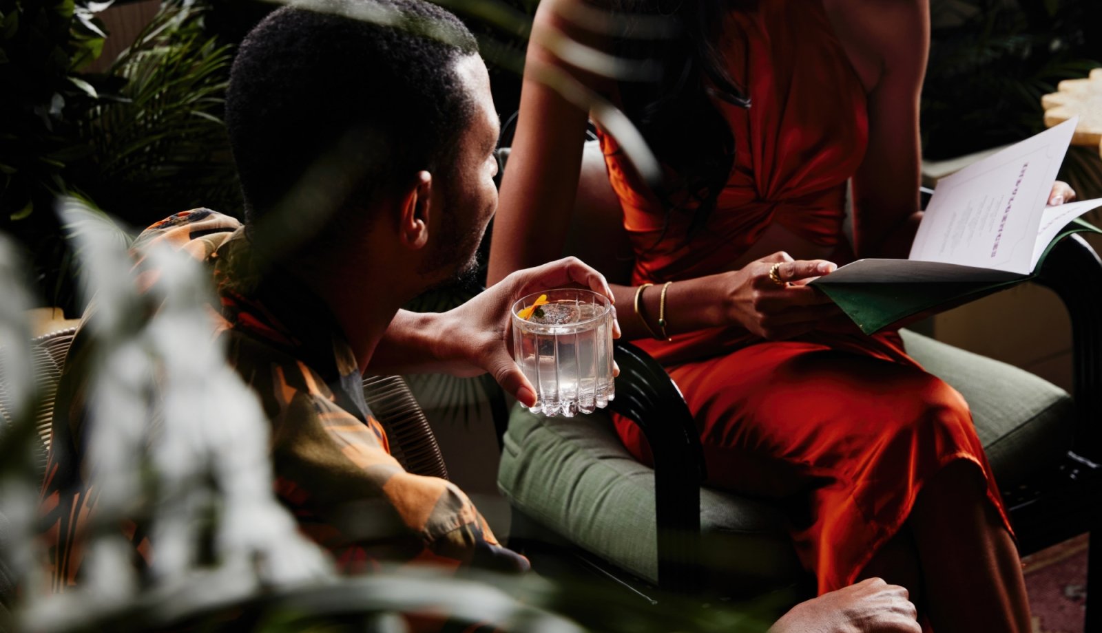 A couple reading a restaurant menu while drinking cocktails.