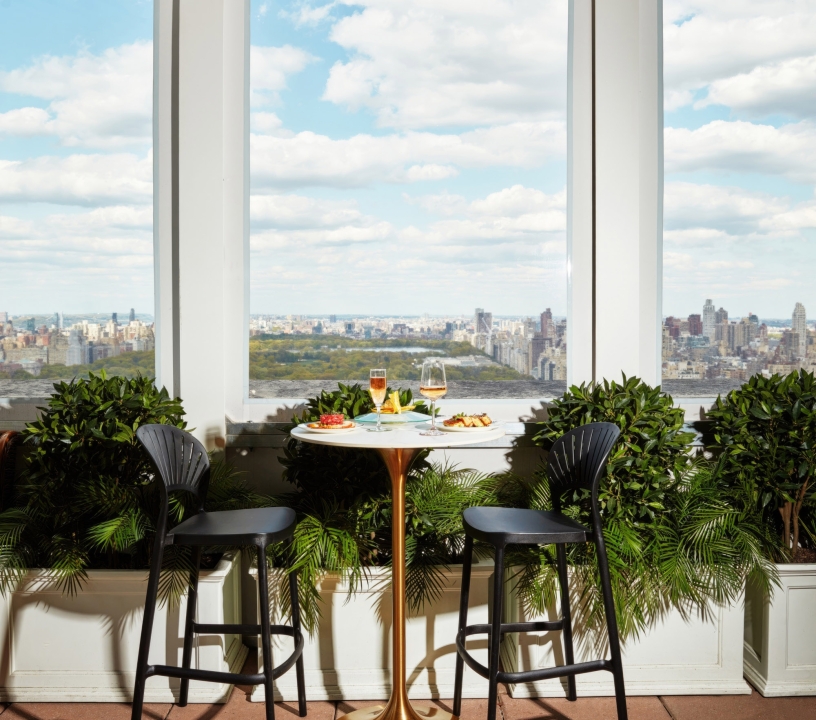 A two-seater table with breakfast by a window overlooking Central Park.