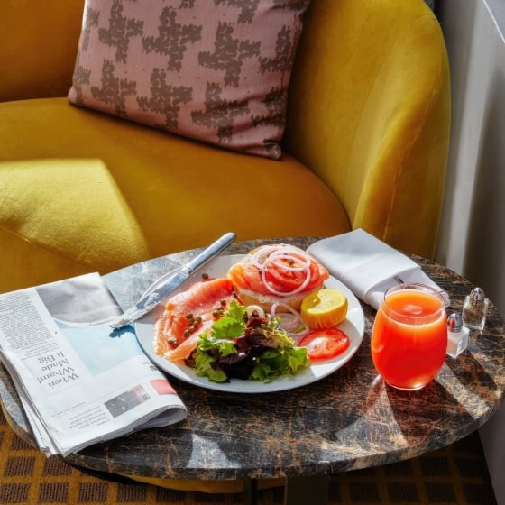 A smoked salmon bagel breakfast with grapefruit juice and a newspaper on a small seating area in a room at Park Lane New York.