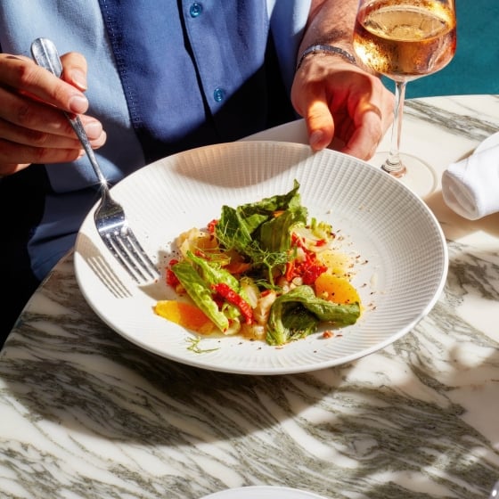 A man eating a salad with a glass of wine.