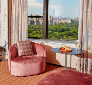 The living area of a suite with pink chairs at Park Lane New York overlooking Central Park.