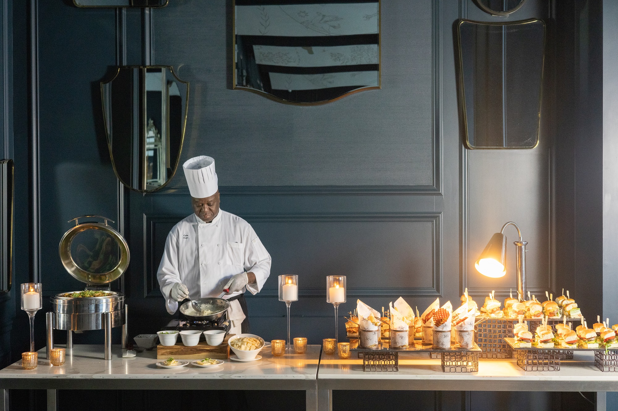 A chef plates a pasta dish on a catering table.