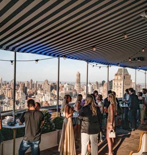 An event space with a view of New York City full of people mingling.