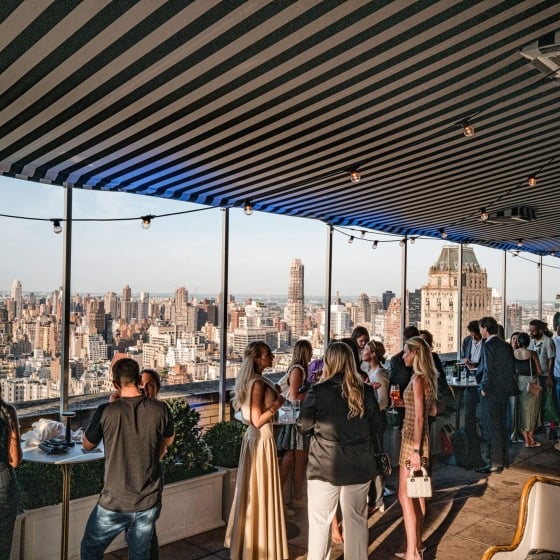 An event space with a view of New York City full of people mingling.