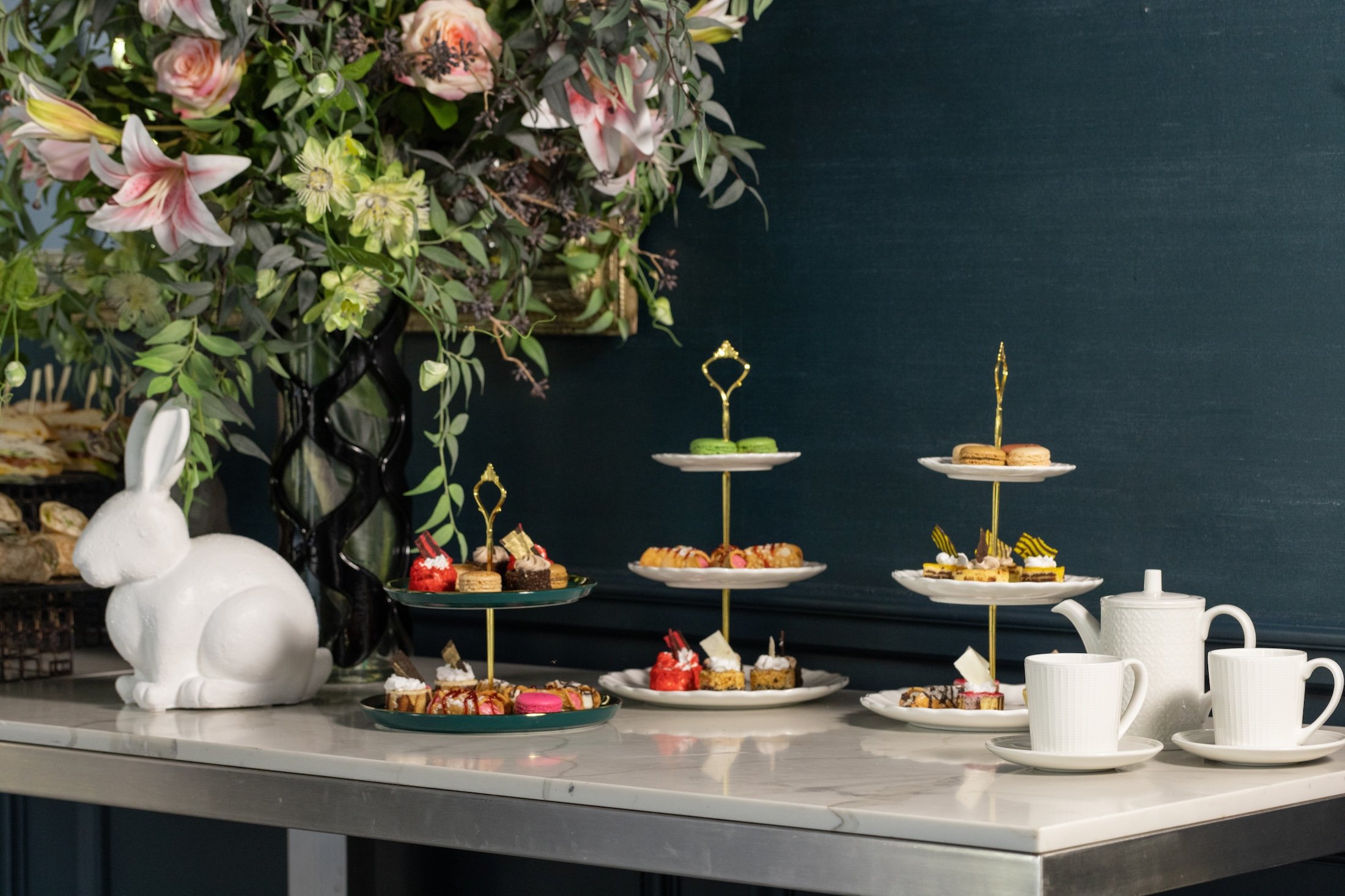 Three tiered trays of desserts on a table with a large bouquet of flowers.