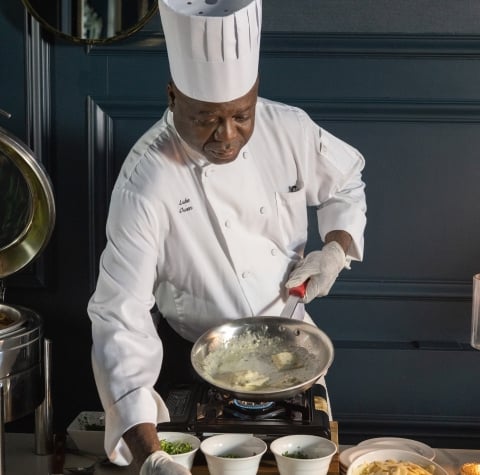 A chef plates a pasta dish on a catering table.