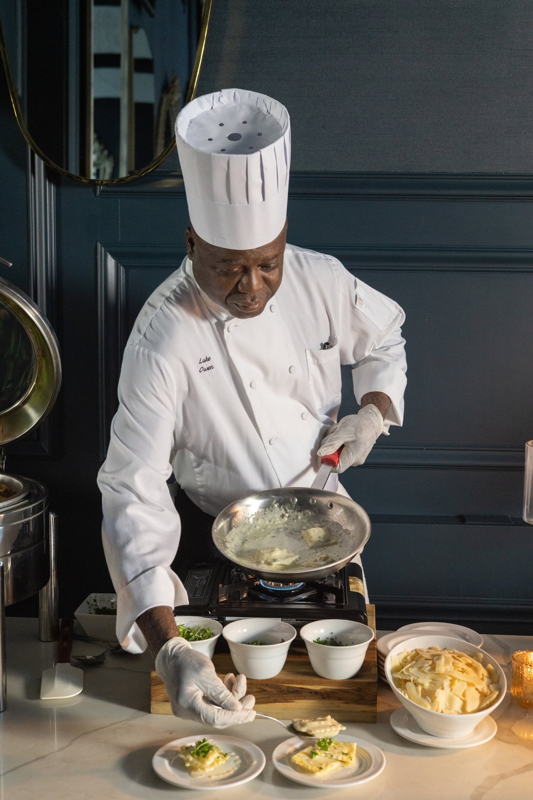 A chef plates a pasta dish on a catering table.