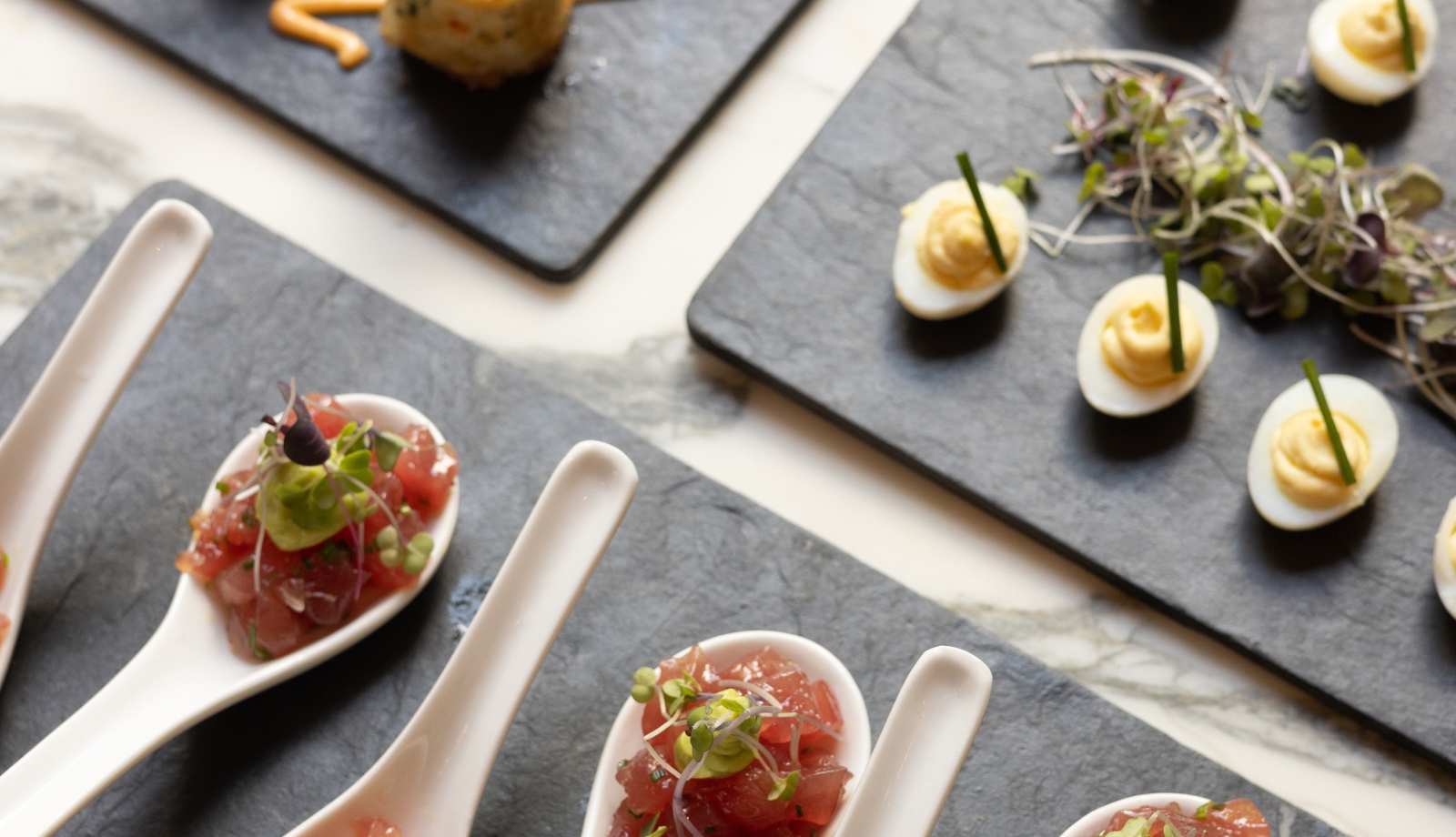 Three trays of hors d'oeuvres including tuna tartare, devilled eggs and croquettes.