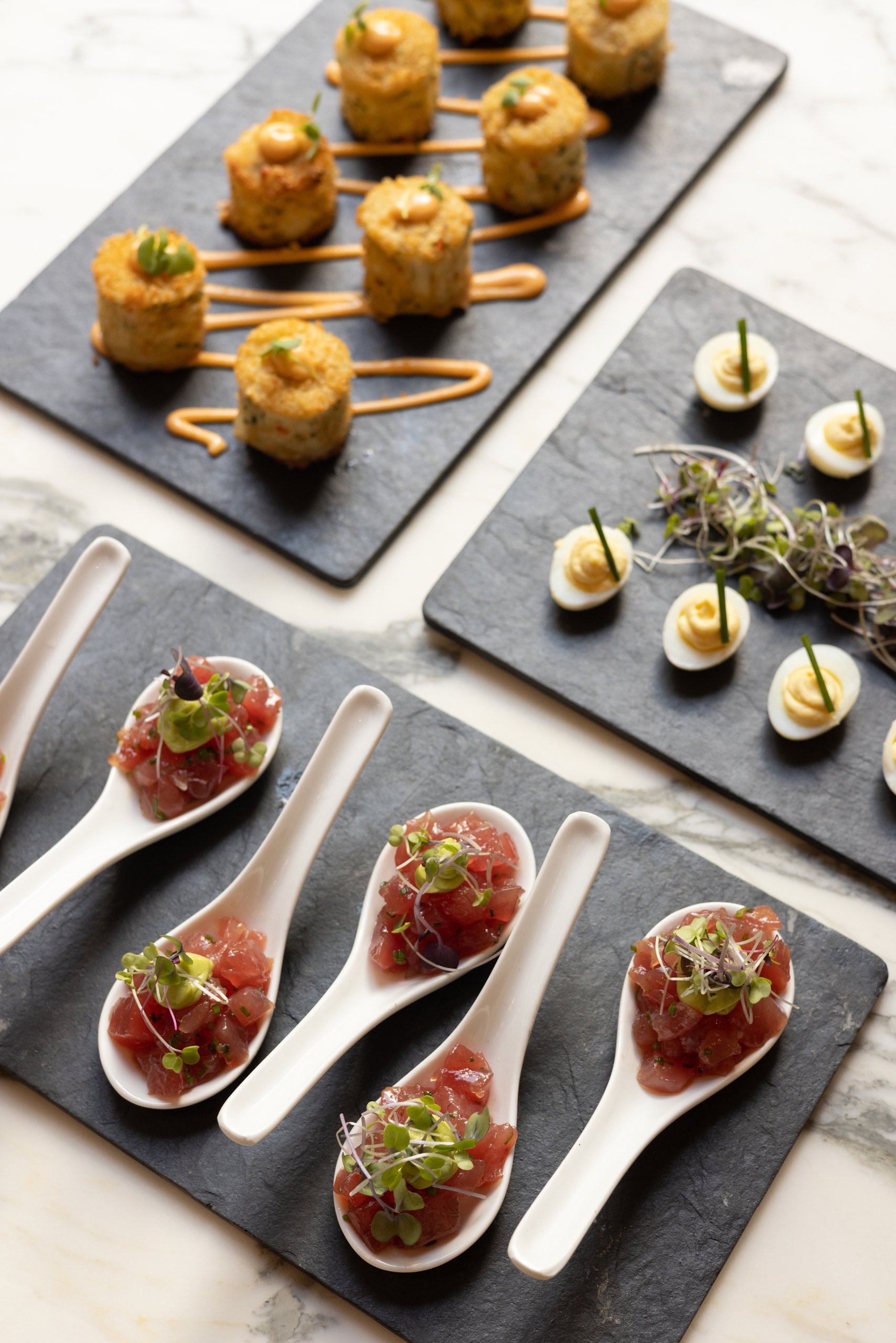 Three trays of hors d'oeuvres including tuna tartare, devilled eggs and croquettes.