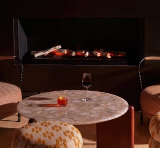 A glass of wine and a cocktail on a table in front of a fireplace.