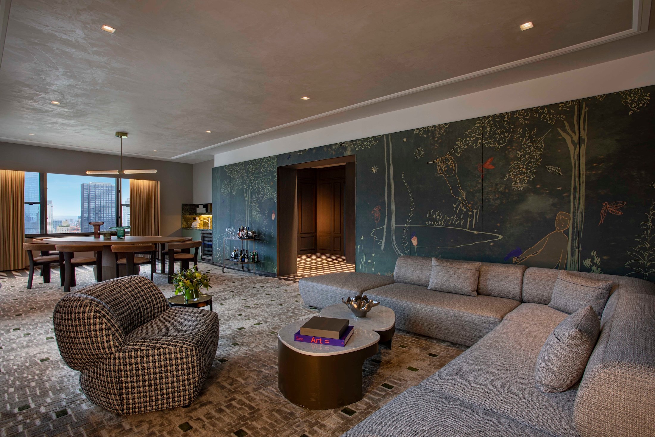 A large living area with sectional couch, dining area and walls with hand painted murals at Park Lane New York.