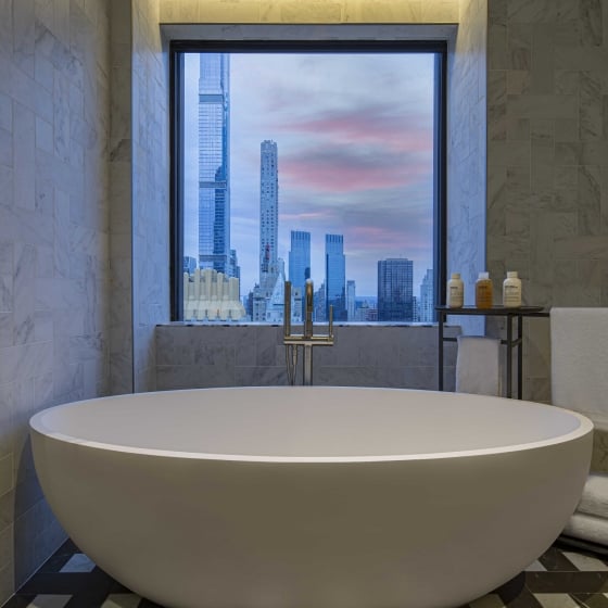 A deep bathtub beneath a window overlooking the New York city skyline in the Conservatory Suite at Park Lane New York.