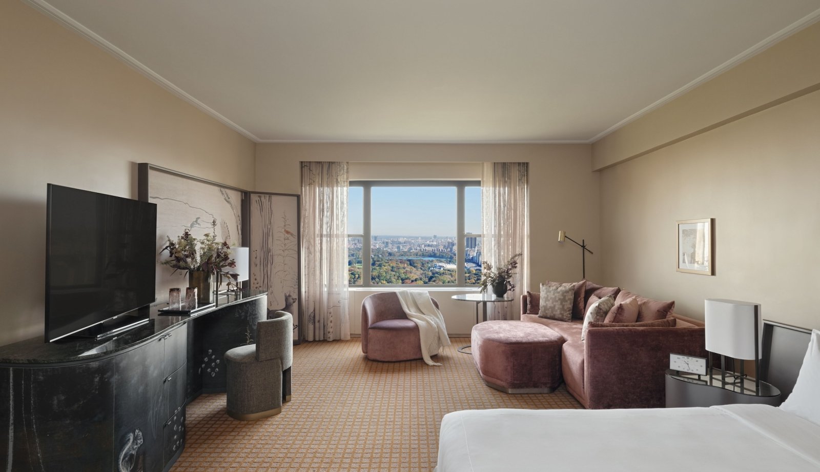 The seating area and king bed of a suite at Park Lane New York with view of Central Park.