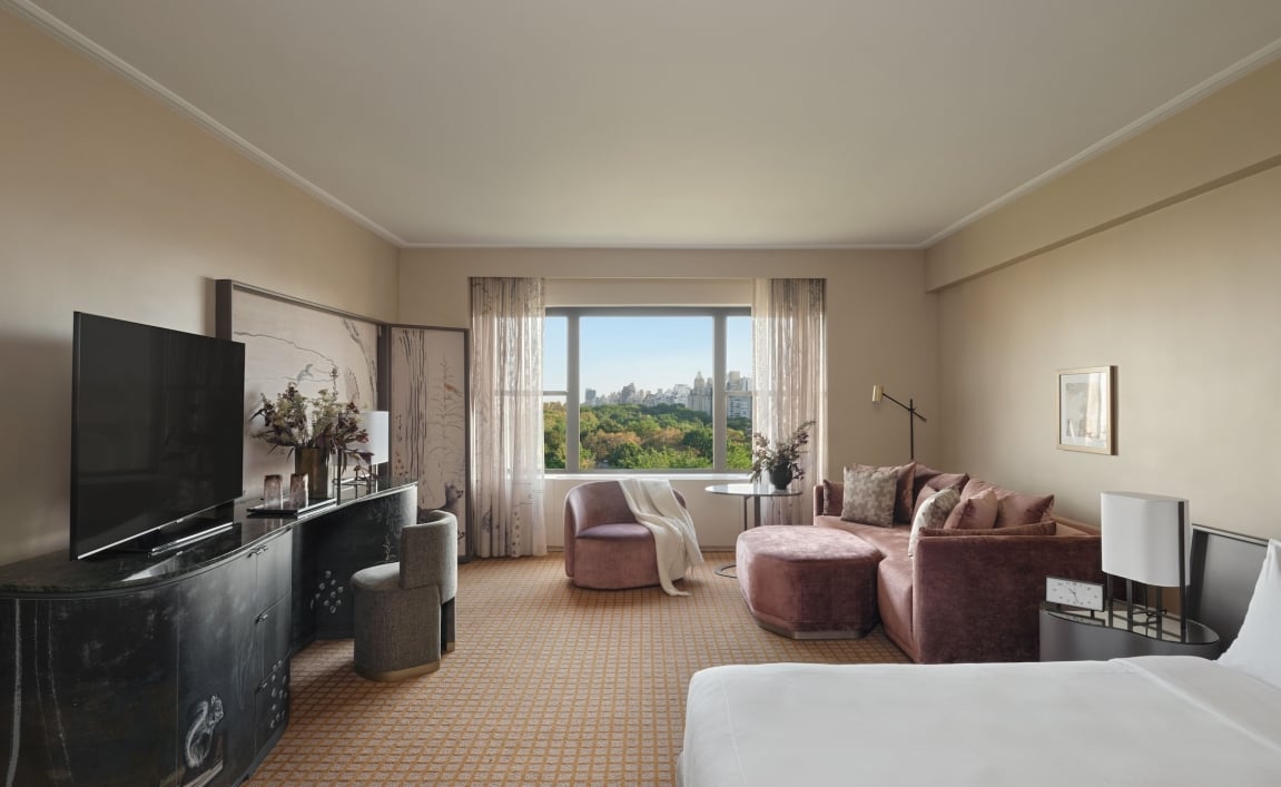 A king bed and seating area including couch, chair and desk in a studio suite overlooking Central Park at Park Lane New York.