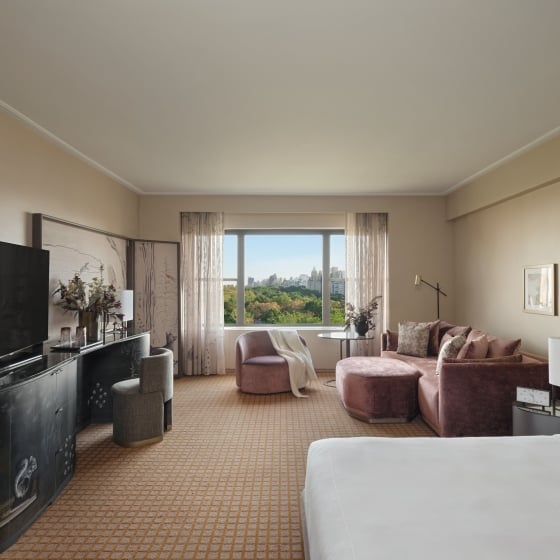 A king bed and seating area including couch, chair and desk in a studio suite overlooking Central Park at Park Lane New York.