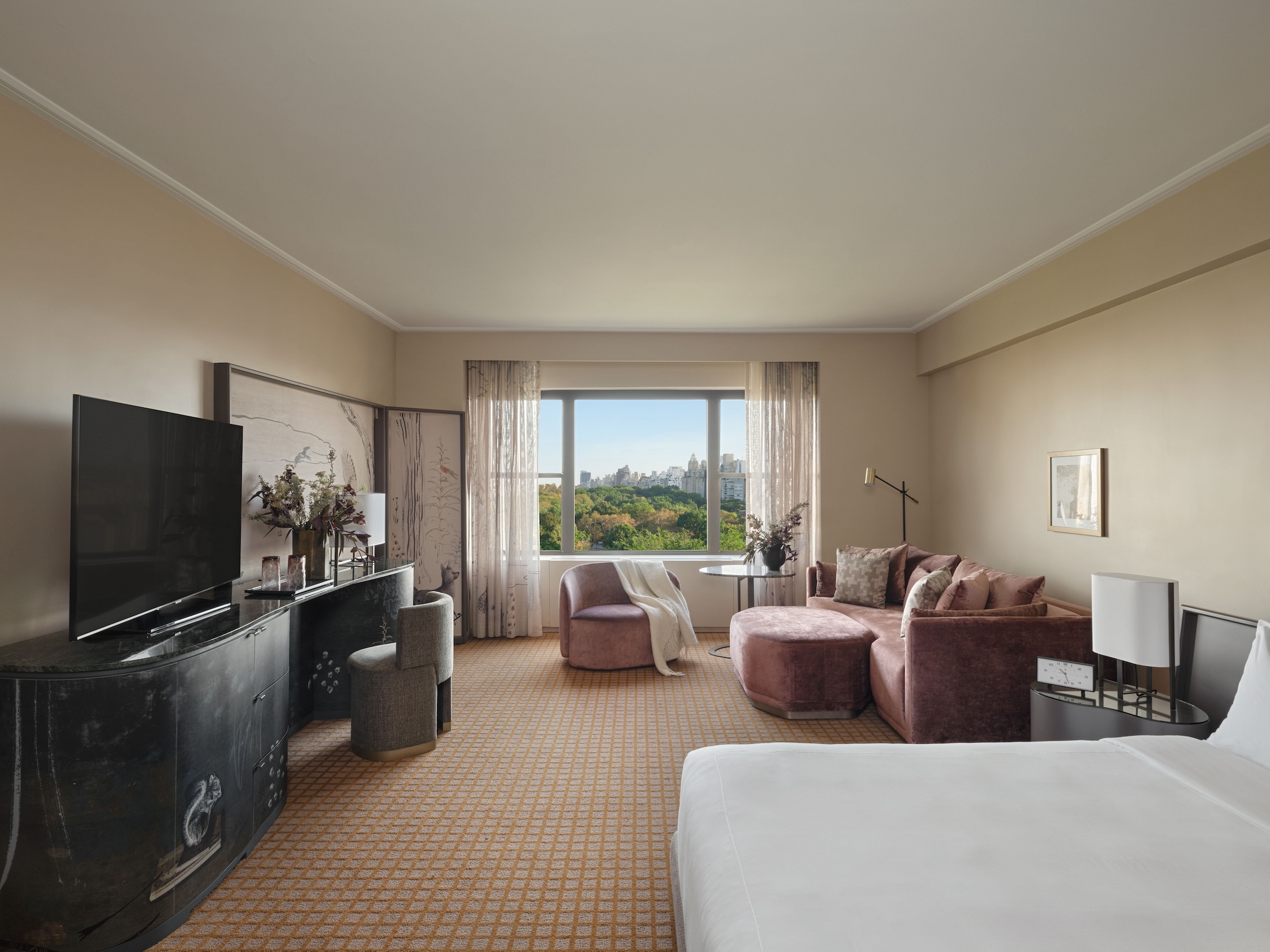 A king bed and seating area including couch, chair and desk in a studio suite overlooking Central Park at Park Lane New York.